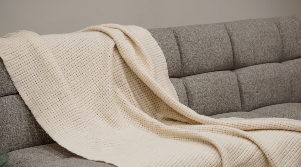 Zoom sur un canapé accueillant avec un plaid, illustrant le confort intérieur d'un appartement neuf à Dagneux.